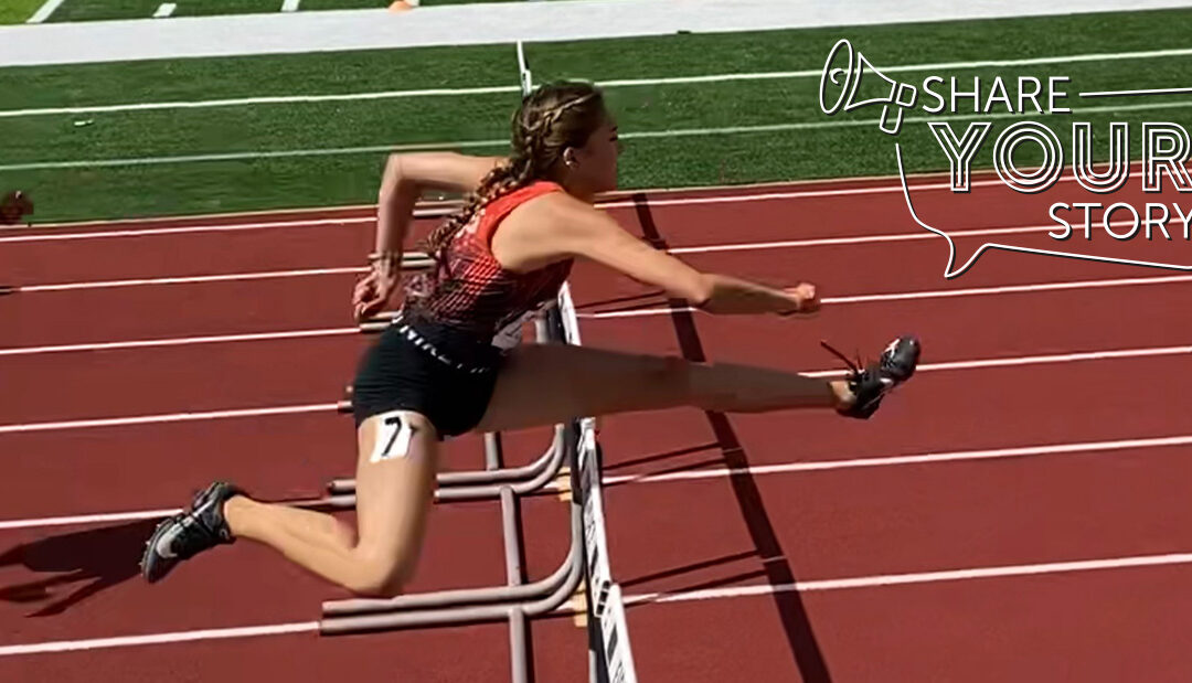 girl jumping over a hurdle on an outside track