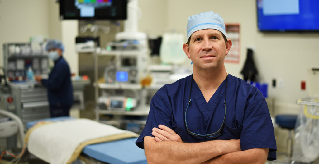 A surgeon stands in an operating room with his arms crossed