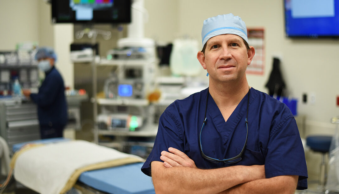 A surgeon stands in an operating room with his arms crossed